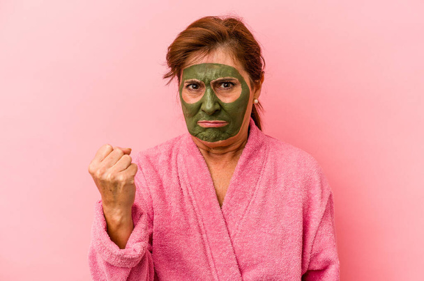 Middle age caucasian woman wearing a facial mask isolated on pink background showing fist to camera, aggressive facial expression. - Fotó, kép