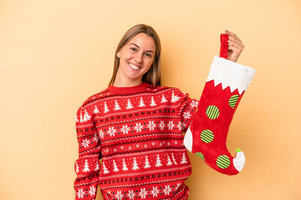 Young caucasian woman holding a elf sock isolated on yellow background happy, smiling and cheerful. - Photo, Image