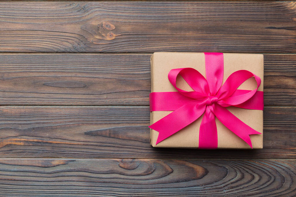 Vakantie geschenkdoos verpakt in ambachtelijk papier met gekleurde strik op tafel achtergrond. Bovenaanzicht, flat lay, kopieerruimte. - Foto, afbeelding