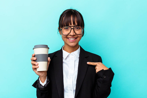 Joven mujer de raza mixta de negocios sosteniendo un café aislado sobre fondo azul persona señalando a mano a un espacio de copia de la camisa, orgulloso y seguro - Foto, imagen