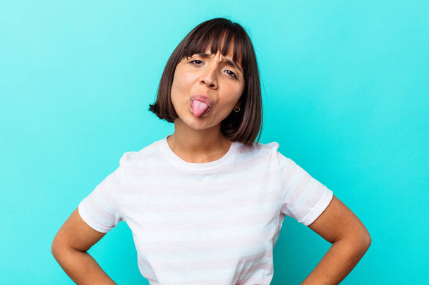 Young mixed race woman isolated on blue background funny and friendly sticking out tongue. - Photo, Image