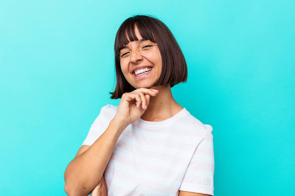 Young mixed race woman isolated on blue background smiling happy and confident, touching chin with hand. - Zdjęcie, obraz