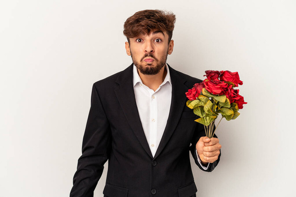 Young mixed race man holding bouquet of roses isolated on white background shrugs shoulders and open eyes confused. - Fotó, kép