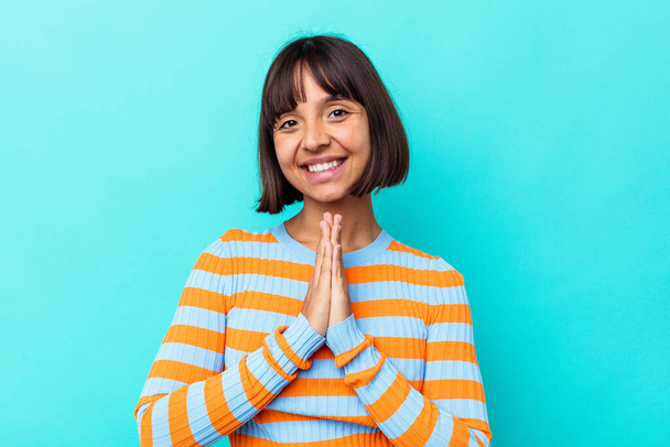 Young mixed race woman isolated on blue background praying, showing devotion, religious person looking for divine inspiration. - Fotografie, Obrázek