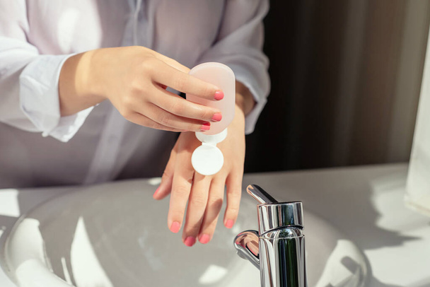 Woman applying cream after washing hands for protective and care dry skin near white sink in bathroom with sunlight from the window.  - Φωτογραφία, εικόνα