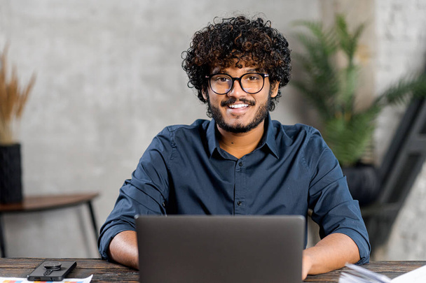 Portrait of smiling and friendly multi ethnic male freelancer in glasses using laptop - Fotó, kép