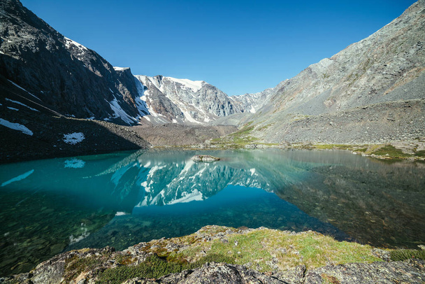 Snowy mountain reflected in clear water of glacial lake. Beautiful sunny landscape with glacier reflection in water surface of mountain lake under clear sky. Snow on rock reflected in mountain lake. - Photo, Image