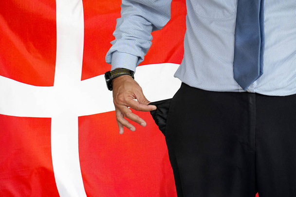 Hand of man in suit turning pocket of his trousers inside out and showing it empty on the background of the Denmark flag. Crisis, unemployment, bankruptcy concept in Denmark - Фото, изображение