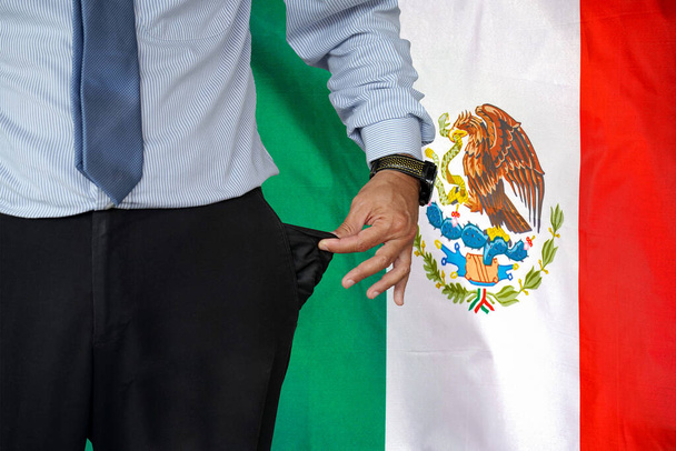 Hand of man in suit turning pocket of his trousers inside out and showing it empty on the background of the Mexico flag. Crisis, unemployment, bankruptcy concept in Mexico - 写真・画像