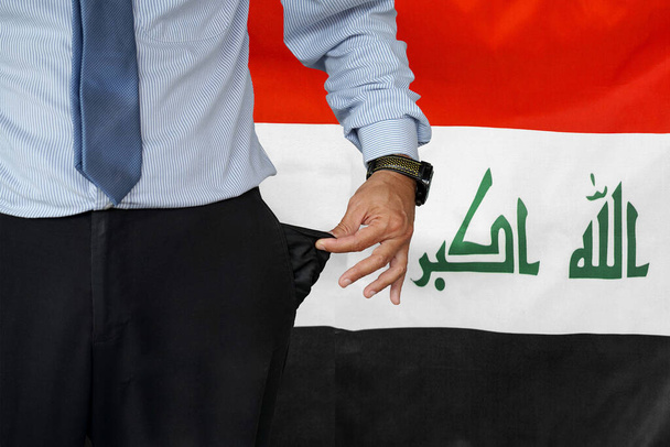 Koura puvussa kääntää housunsa ylösalaisin ja näyttää ne tyhjinä Irakin lipun alla. Kriisi, työttömyys, konkurssi Irakissa - Valokuva, kuva