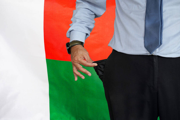Hand of man in suit turning pocket of his trousers inside out and showing it empty on the background of the Madagascar flag. Crisis, unemployment, bankruptcy concept in Madagascar - Fotografie, Obrázek