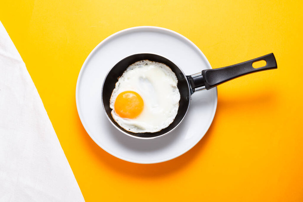 Scrambled, frying  eggs from one egg in a small pan on yellow ba - Foto, Imagem