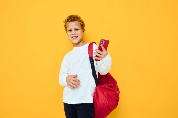 portrait of a little boy with a red backpack calls on the phone Studio learning concept - 写真・画像