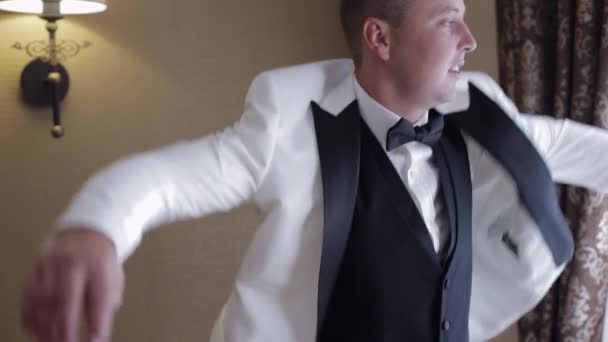Bello uomo elegante sposo indossa giacca bianca a casa in soggiorno, rallentatore al coperto ritratto - Filmati, video