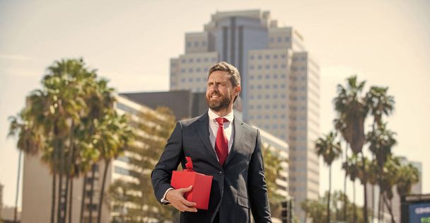 uomo d'affari barbuto sorridente in formalwear tenere scatola regalo fuori dall'ufficio, acquisto - Foto, immagini