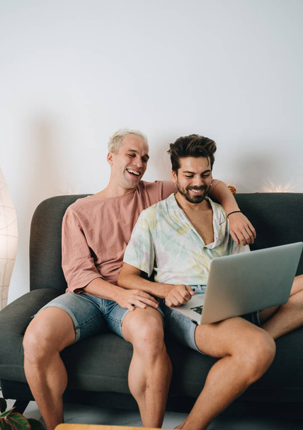 Gay couple sitting on sofa with laptop in their house - Zdjęcie, obraz