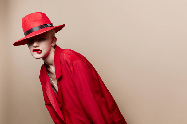 Kırmızı ceketli ve şapkalı bir kadının portresi. Kırmızı dudaklar, bej arka plan. - Fotoğraf, Görsel