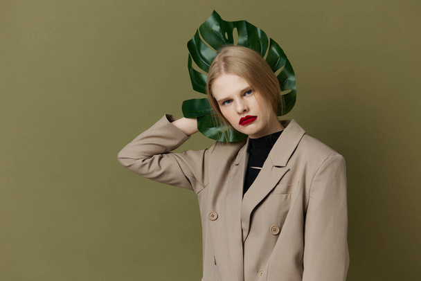 blond vrouw in jas rood lippen mode palm blad groen achtergrond - Foto, afbeelding