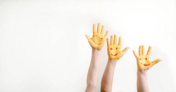 Close children's hands painted with yellow paint gouache with smile faces on it on white background. Free space for text copyspace - 写真・画像