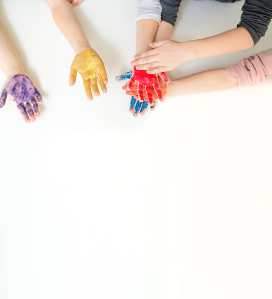 Close children's hands painted with yellow, blue pink, purple and orange paint gouache with on white background. Free space for text copy space - 写真・画像