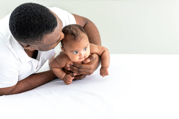 Afrikai apa öleli és védi a lányát, 3 hónapos baba újszülött, amely mosolyog és boldog egy fehér hálószoba, az afrikai család és újszülött koncepció. - Fotó, kép