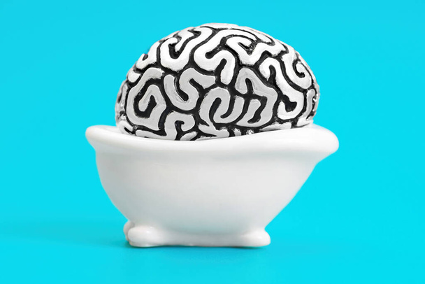 Steel copy of a human brain lying in a toy bath tub isolated on a blue background. Hot tub soaking for the mood lift. - Photo, image