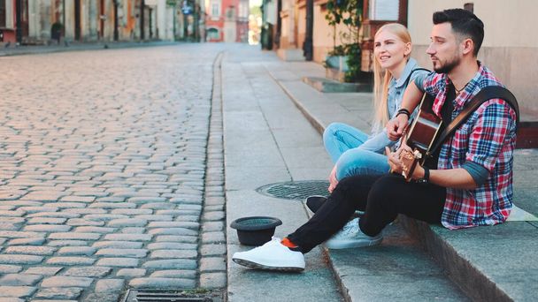 Jeune couple de chanteurs de rue dans la vieille partie de la ville assis sur le trottoir - Photo, image