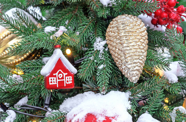 Pequeña cabaña roja de Navidad y cono de pino dorado en el árbol de Navidad. - Foto, imagen