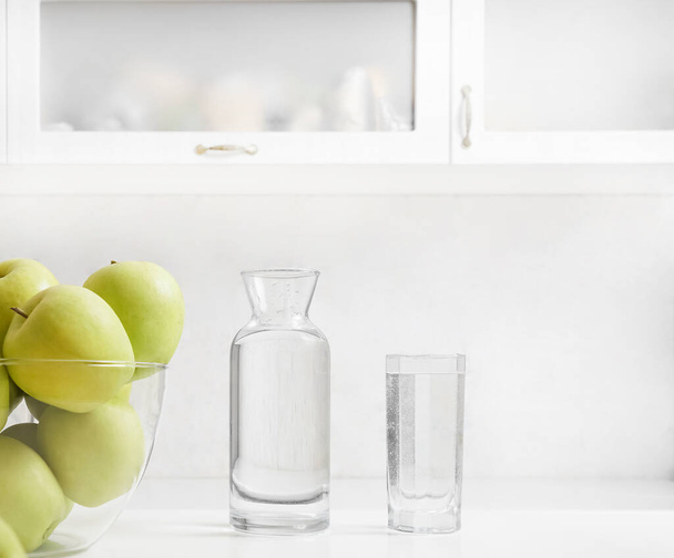 Freshly washed apples on the kitchen table. bottle and full glass of water on cupboard background. interior backdrop.  - Foto, imagen