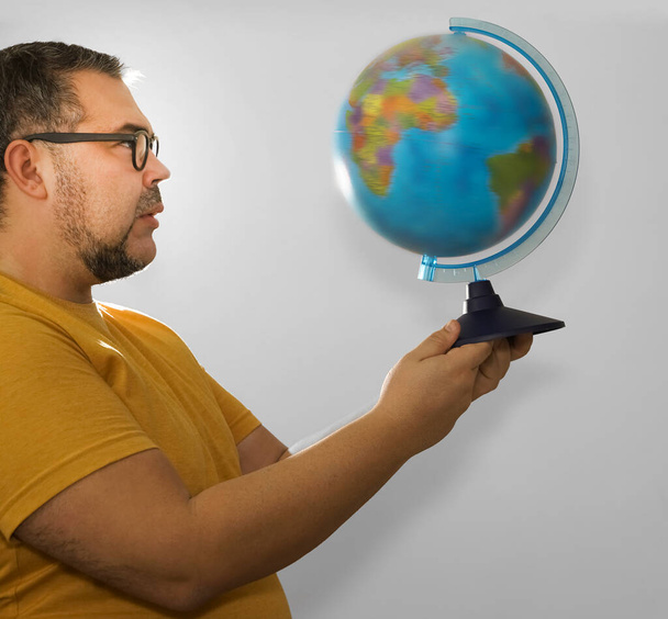 Young caucasian bearded geography student traveler indignant man in yellow basic t-shirt hold in hands Earth world globe. Male looking at globe map isolated on grey background. studio shot.  - Фото, изображение