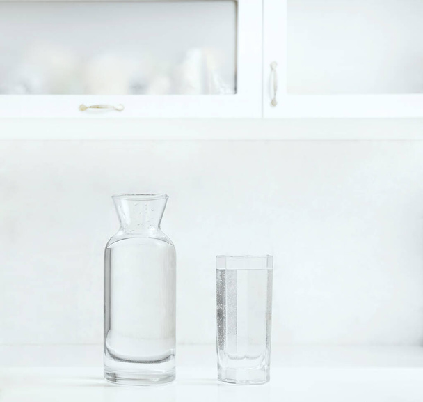 jar, bottle of water with full transparent glasses on white table. - Foto, Imagen