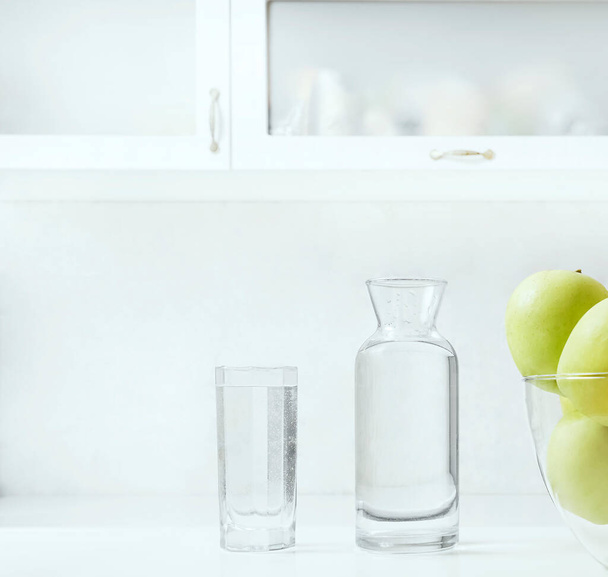 Freshly washed apples on the kitchen table. bottle and full glass of water on cupboard background. interior backdrop.  - Foto, Imagen