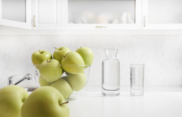 Freshly washed apples on the kitchen table. bottle and full glass of water on cupboard background. interior backdrop.  - Photo, Image