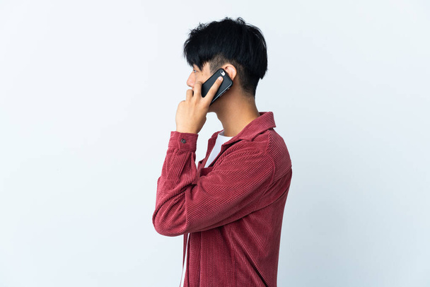 Young Chinese man isolated on white background keeping a conversation with the mobile phone with someone - 写真・画像