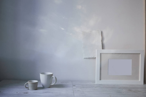 Scandinavian style. Interior Design. A white cups of different size, a frame for a photo are on the table. the blank sheets of paper are attached to the wall. Empty space for text - Photo, Image