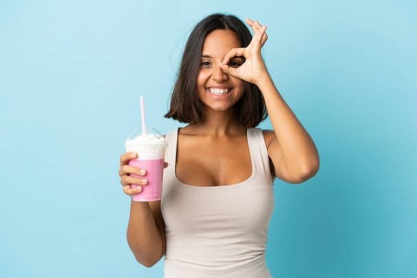 Jeune femme avec milkshake fraise isolé sur fond bleu montrant ok signe avec les doigts - Photo, image