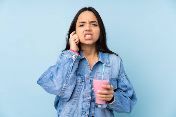 Молода жінка з полуничним молочним коктейлем над ізольованим синім тлом розчарована і покриває вуха
 - Фото, зображення