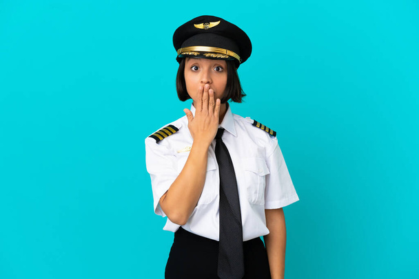 Νεαρός πιλότος αεροπλάνου πάνω από απομονωμένο μπλε φόντο καλύπτει το στόμα με το χέρι - Φωτογραφία, εικόνα