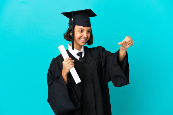 Joven universitaria graduada sobre aislado fondo azul dando un gesto pulgares hacia arriba - Foto, imagen