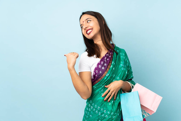 Jovem indiana com sacos de compras apontando para o lado para apresentar um produto
 - Foto, Imagem