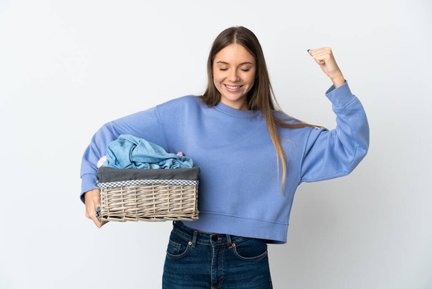 Young Lithuanian woman holding a clothes basket isolated on white background doing strong gesture - Fotó, kép