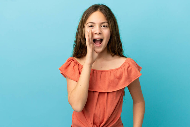 Little caucasian girl isolated on blue background shouting with mouth wide open - Foto, Imagen