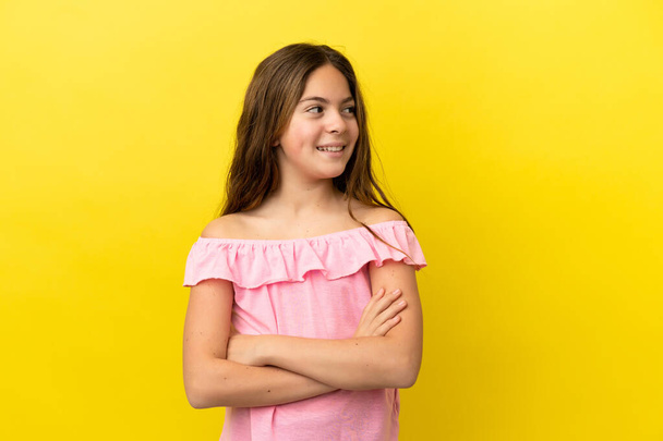 Little caucasian girl isolated on yellow background with arms crossed and happy - Fotografie, Obrázek