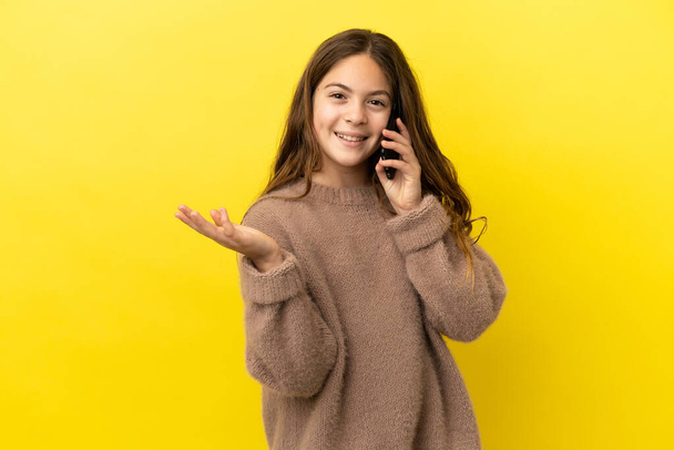 Little caucasian girl isolated on yellow background keeping a conversation with the mobile phone with someone - Foto, afbeelding