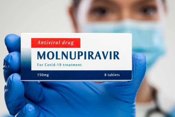 Tıbbi çalışanlar ilaç paketini tutuyor, MOLNUPIRAVIR klinik deney antiviral ilaç geliştirme aşamasında, Coronavirus enfeksiyonu için tedavi, COVID-19 virüs önleme ve koruma, illüstrasyon - Fotoğraf, Görsel