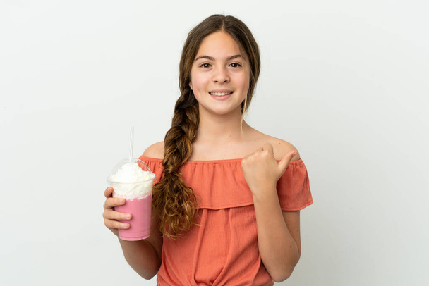 mała kaukaska dziewczyna z truskawkowy milkshake izolowane na białym tle wskazując na stronie przedstawić produkt - Zdjęcie, obraz