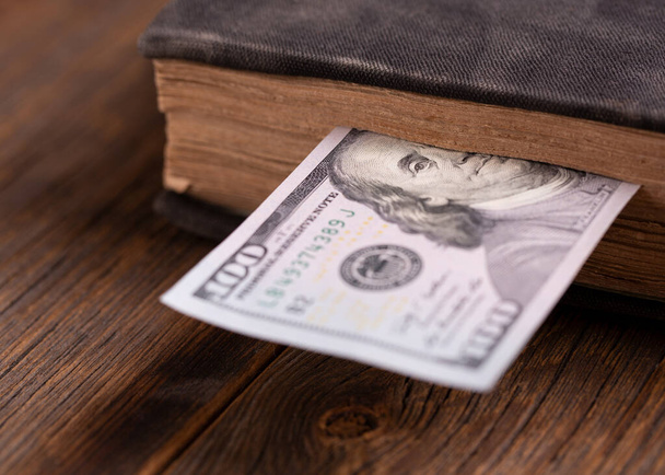 Hundred dollar bill inserted in an old book. Hundred dollar bill and book on a wooden table. - Foto, imagen