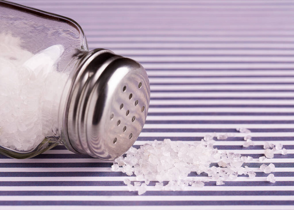 A bunch of salt and a salt shaker lying on its side. Salt in the kitchen. - Fotografie, Obrázek