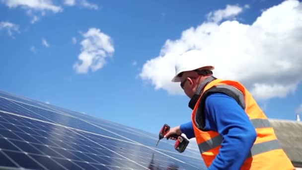 Άνδρας εργαζόμενος σε ανακλαστικό γιλέκο και προστατευτικό κράνος λειτουργεί γεώτρηση στον ηλιακό πίνακα. Μηχανικός που δουλεύει στη φάρμα ηλιακών συλλεκτών. Επισκευή και συντήρηση οικολογικών πηγών ενέργειας - Πλάνα, βίντεο