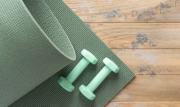 Green dumbbells and the green sports mat on the wooden floor - Fotografie, Obrázek